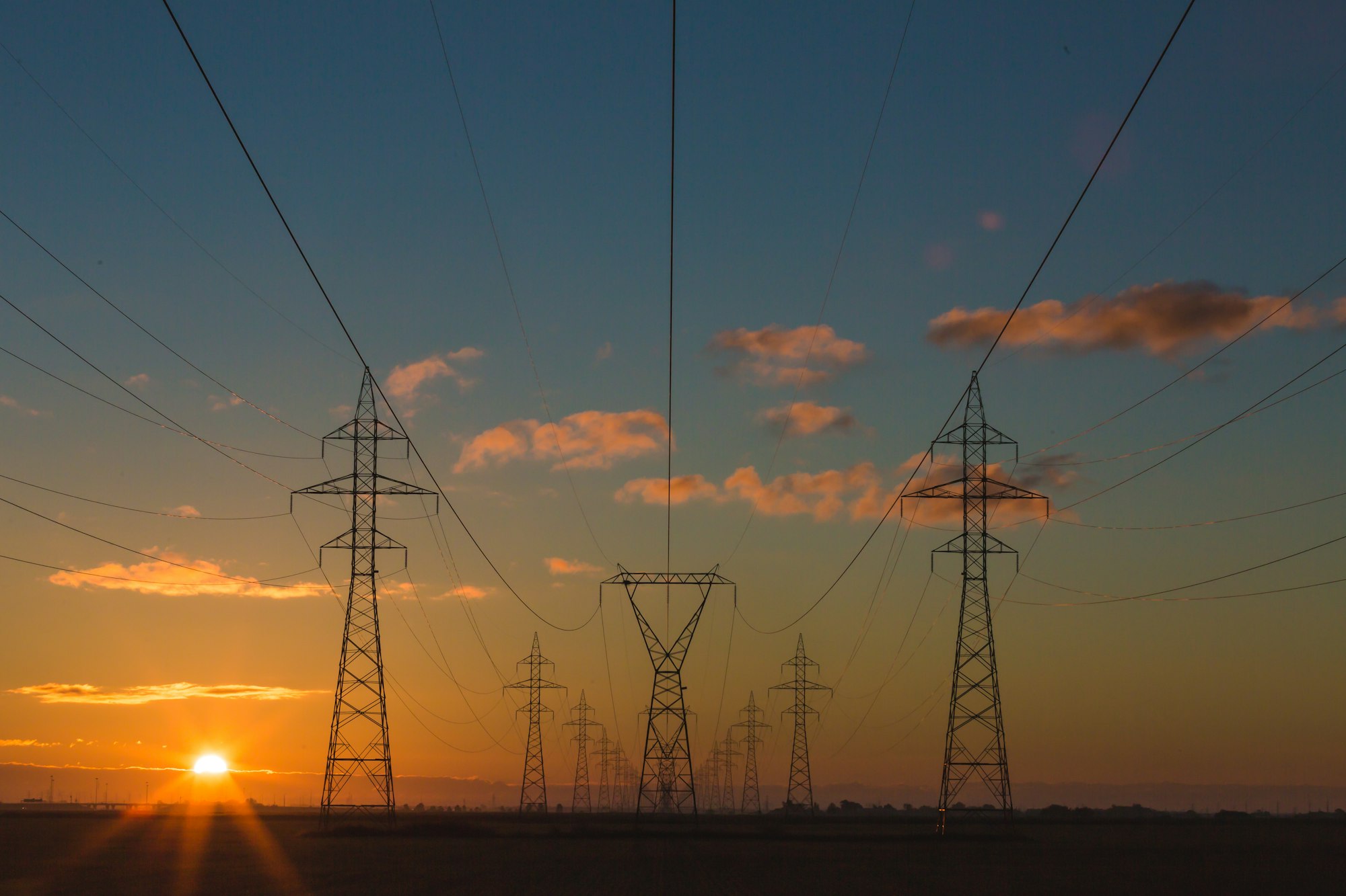 Power lines and lighting at dusk under an orange sky