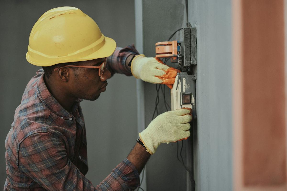 Electrician in a hard hat working on a wall-mounted electrical unit